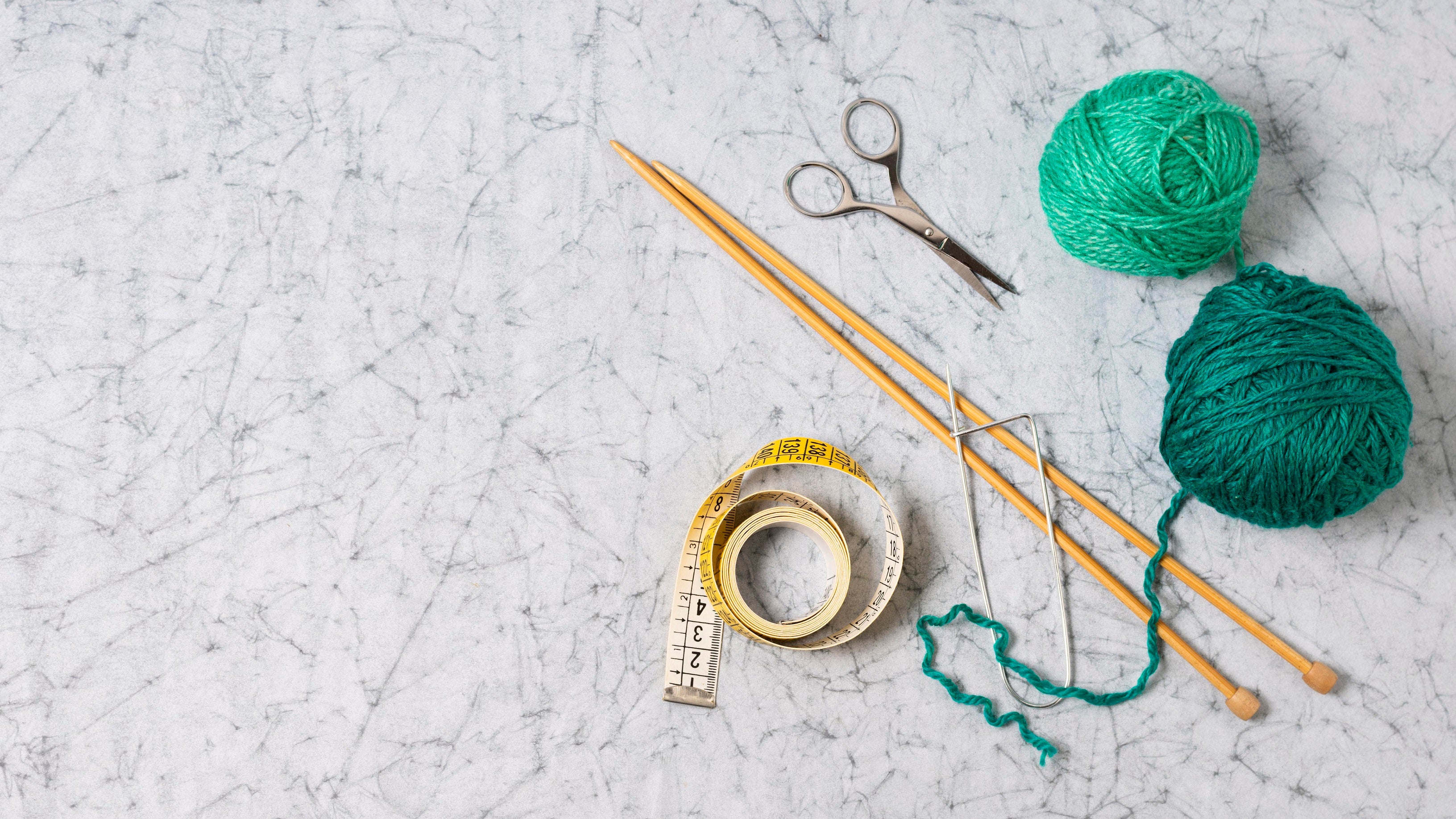 Knitting needles, yarn, scissors, and measuring tape arranged on a table